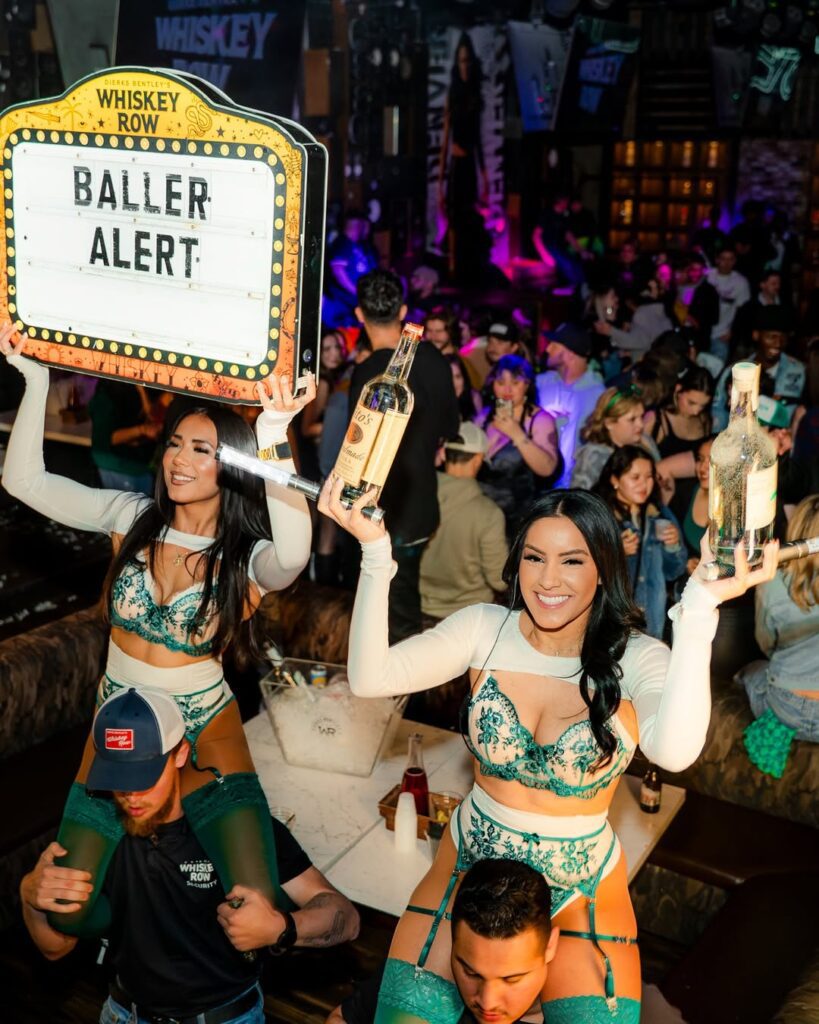 Bar girls holding bottles at Dierks Bentley's Whiskey Row Nashville, celebrating with VIP bottle service.