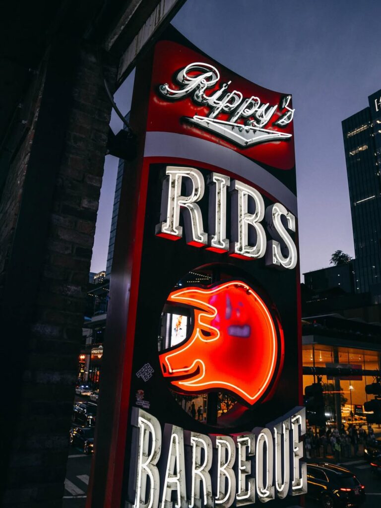 Neon sign for Rippy’s Ribs Barbeque in downtown Nashville featuring a glowing pig icon and bold lettering at dusk