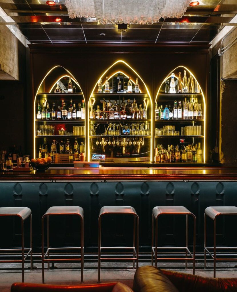 Chic illuminated bar shelves with bottles and cocktails at Hidden Bar in Nashville.