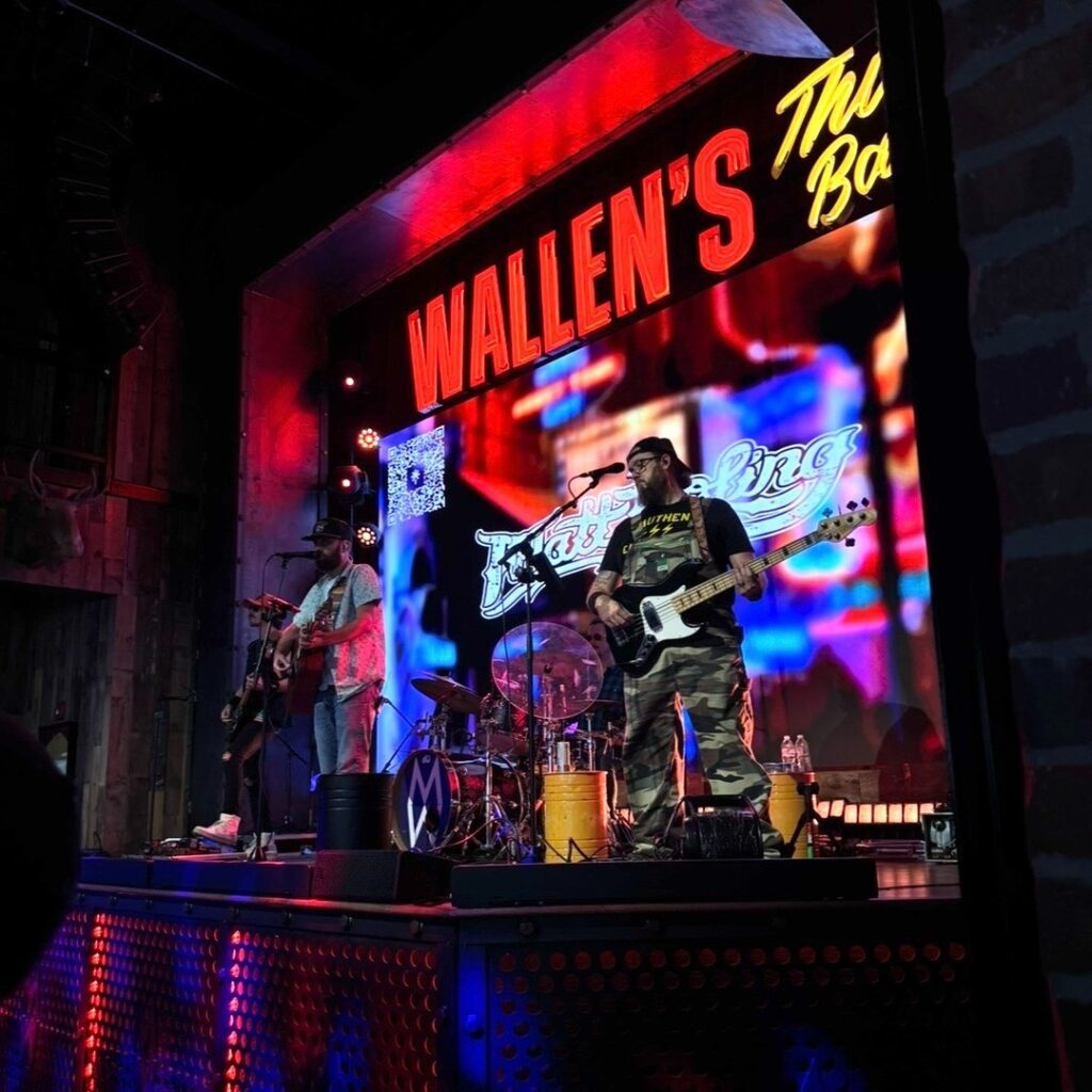 Interior view of Morgan Wallen's This Bar & Tennessee Kitchen, showcasing a lively performance on the main level with a crowd enjoying live music, rustic Tennessee decor, exposed brick walls, and vibrant lighting, capturing the energetic honky tonk atmosphere.