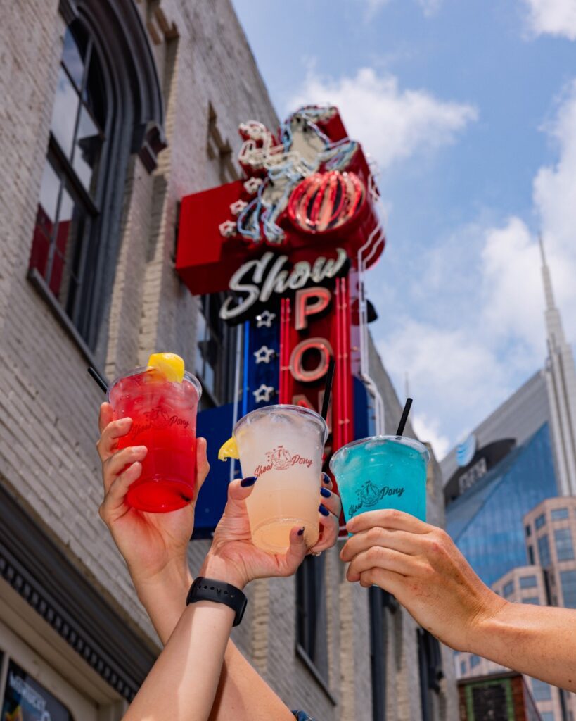 Colorful cocktails held up in front of the neon Show Pony sign on Broadway in Nashville.