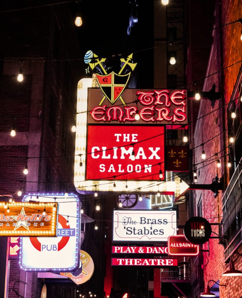 Neon signs light up Nashville’s Printer’s Alley, showcasing The Climax Saloon, The Embers, karaoke bars, and late-night venues.