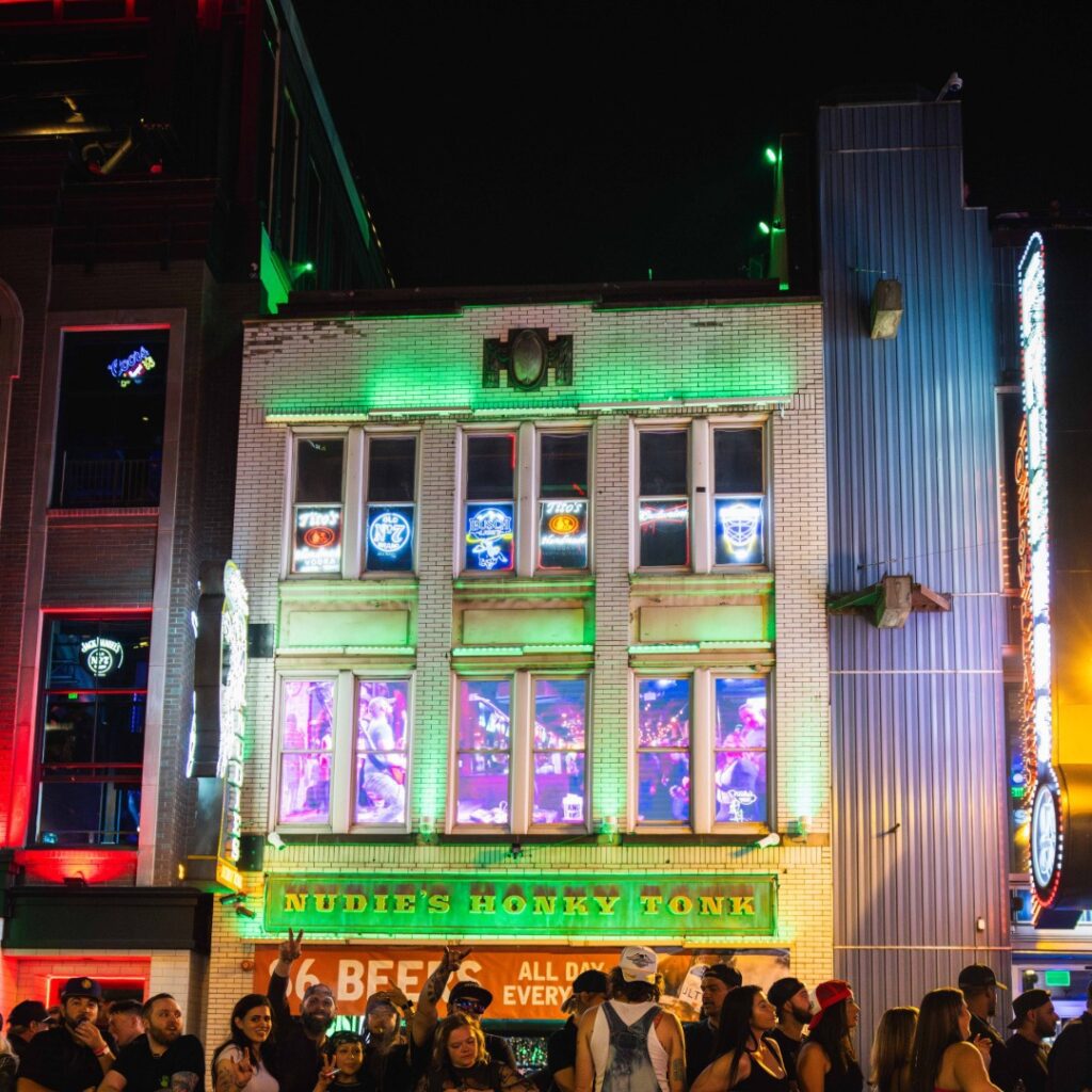 Crowds outside Nudie’s Honky Tonk on Broadway in downtown Nashville, with neon lights and live music glowing from the windows.