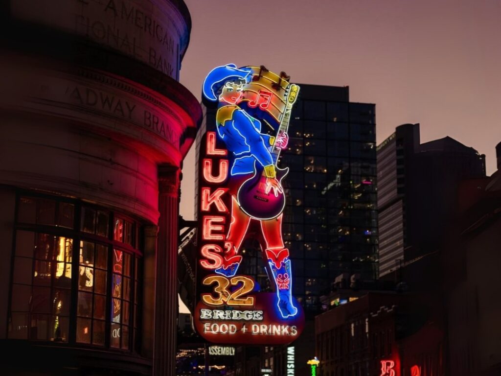 Neon sign of Luke’s 32 Bridge bar in downtown Nashville featuring a guitar-playing cowboy figure against a city skyline