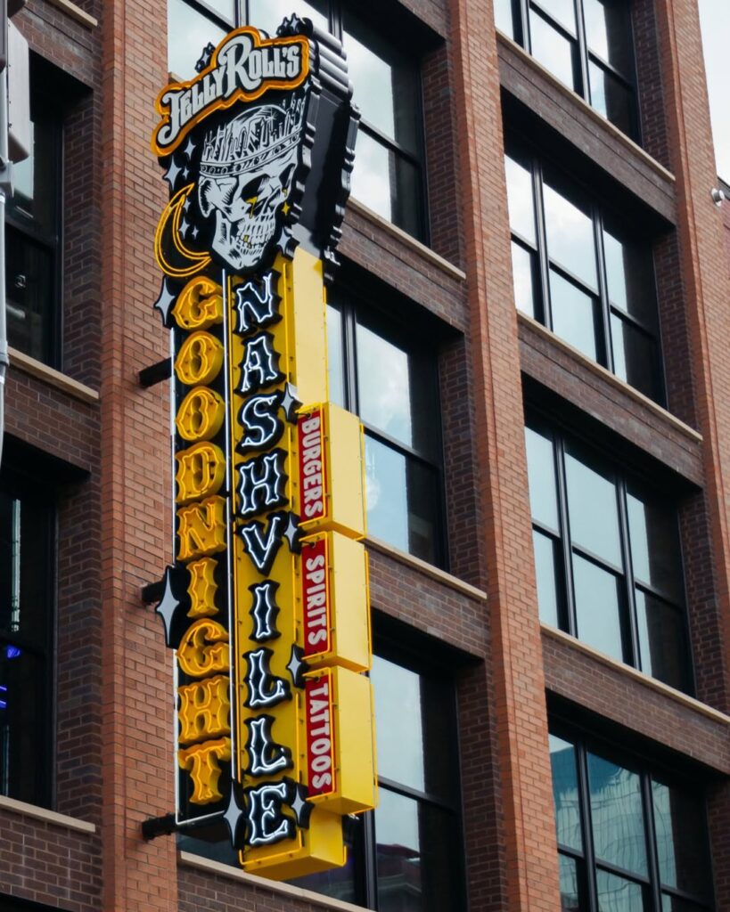 Exterior neon sign of Jelly Roll’s Goodnight Nashville bar on Broadway, featuring a skull logo and bright yellow and black lettering.