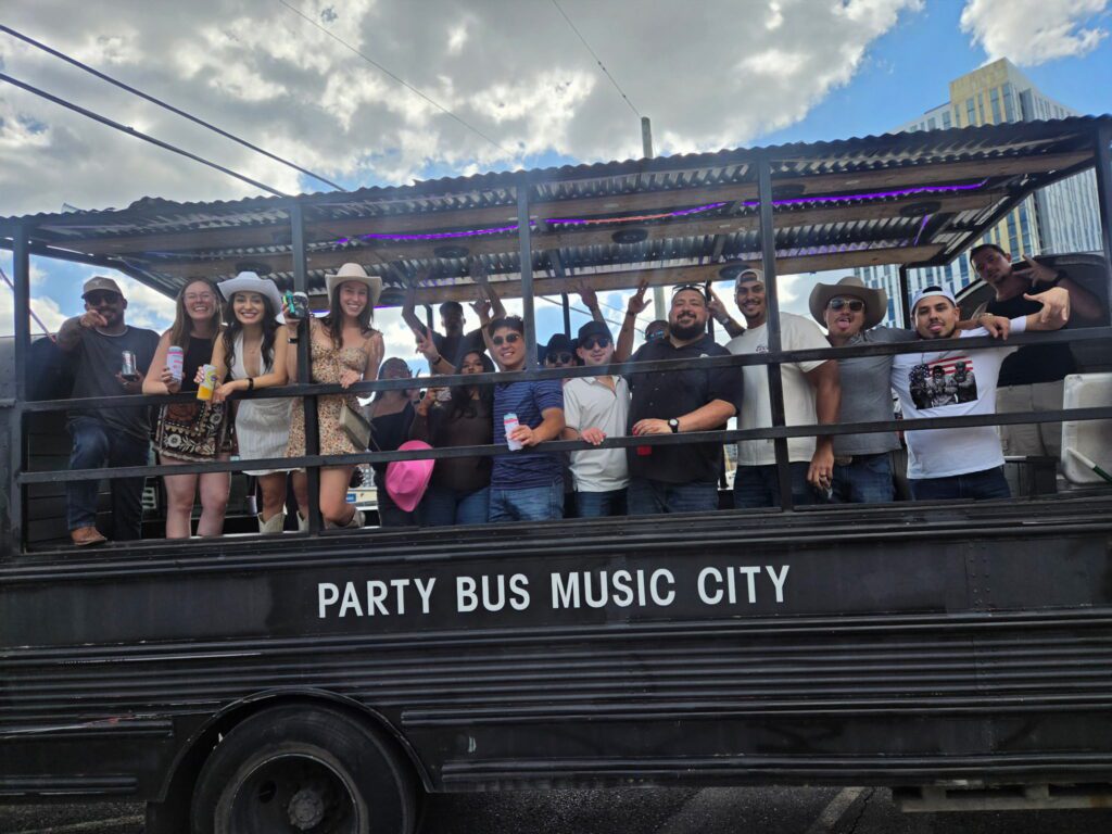Class reunion sized group waving from a Rowdy Bus with the Nashville skyline behind